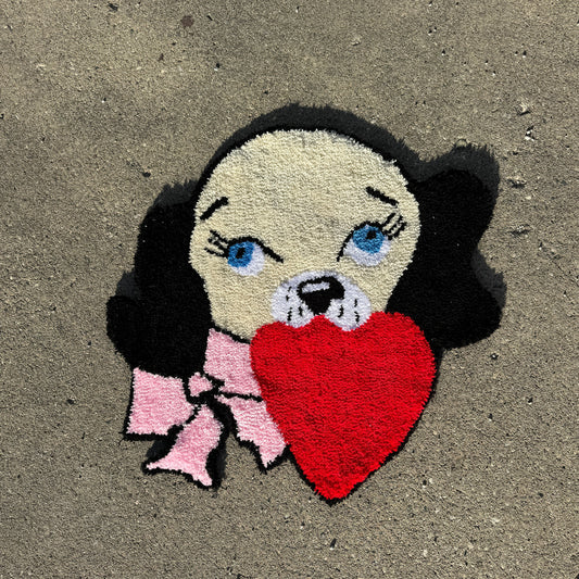 A charming tufted rug depicting a black-eared dog with a heart in its mouth and a pink bow, showcasing intricate craftsmanship on a textured concrete background.